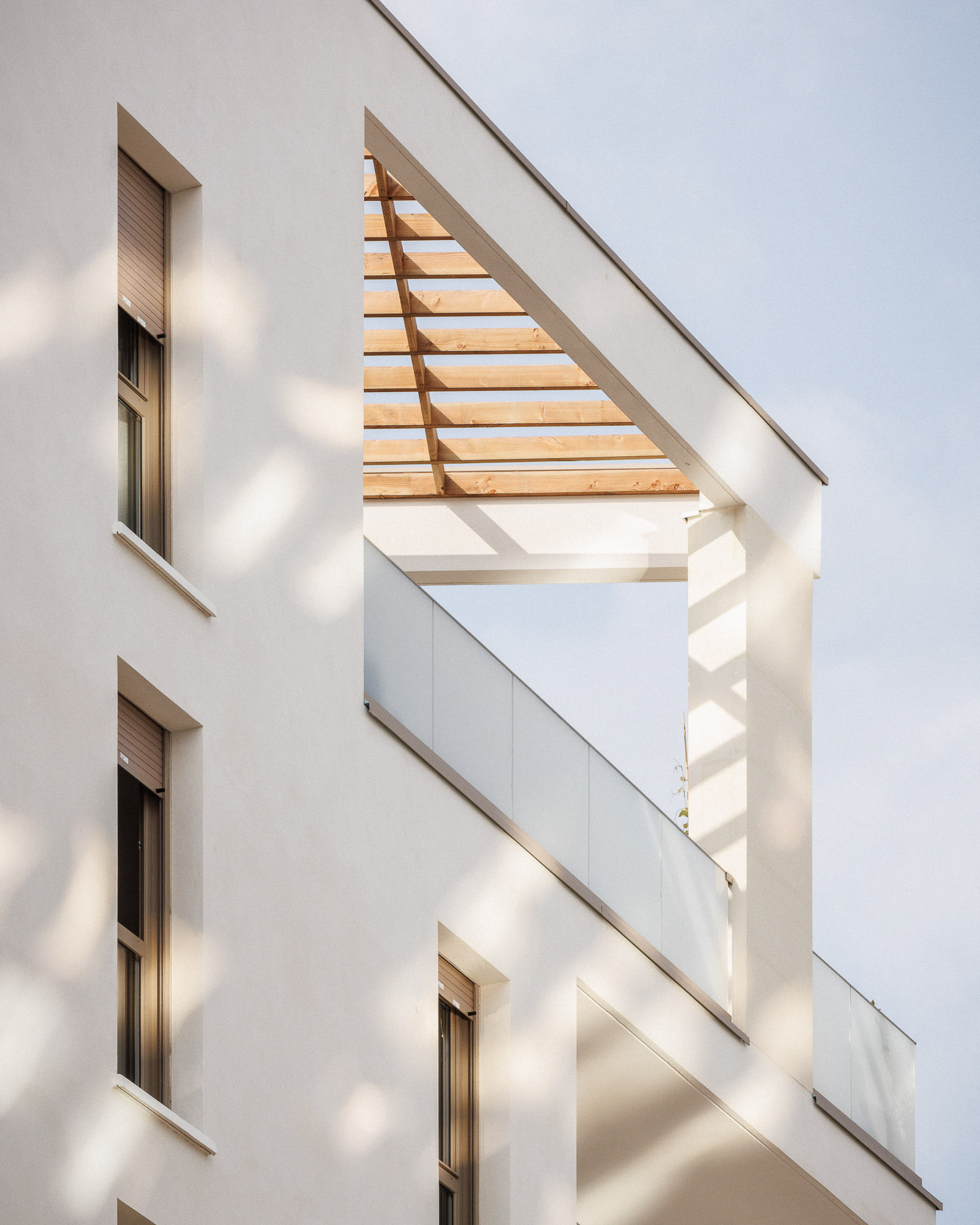 Aperçu d'une terrasse d'un logement avec pergola en bois et garde corps vitré en angle d'un bâtiment en pierre